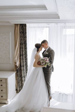 Gelin ve damat pencerenin önünde el ele tutuşup birbirlerine bakıyorlar.