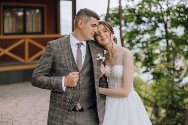 Gelin ve damat kulübenin dışında ellerinde çiçekle bekliyorlar. Sahne romantik ve samimi.