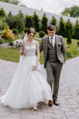 Bir gelin ve damat yolda yürüyorlar, gelin bir buket tutuyor ve damat bir takım elbise giyiyor.