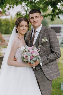 Bir gelin ve damat bir buket çiçekli fotoğraf için poz veriyorlar. Gelin beyaz bir elbise giyiyor ve damat bir takım elbise giyiyor. Sahne mutlu ve kutlama dolu.