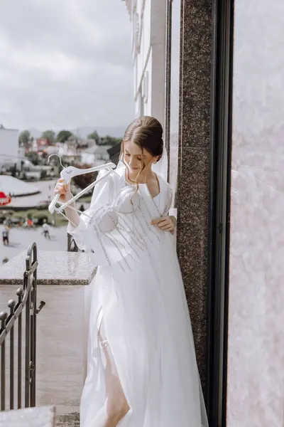 女性は白いドレスを着て白いドレスハンガーを抱えているバルコニーの上に立っている 彼女はカメラを見ている ストック画像