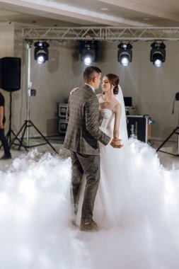 Bir gelin ve damat etraflarında dumanla havada dans ediyor. Sahne romantik ve rüya gibi.