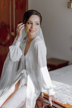 Beyaz elbiseli bir kadın yatağa oturur. Gülümsüyor ve kameraya bakıyor.