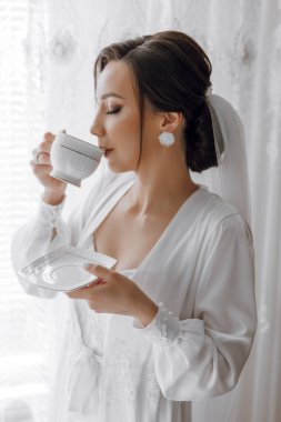 Beyaz cüppeli bir kadın beyaz bir fincandan çay içiyor. Huzurlu ve huzurlu bir manzara, kadın sessiz bir ortamda çayını içiyor.