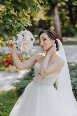 Beyaz elbiseli bir kadın peçe takıyor ve elinde bir buket çiçek tutuyor. Düğün için hazırlanıyor.