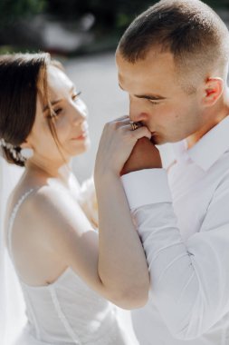 Bir erkek ve bir kadın, kadının elini tutan adamla kucaklaşıyorlar. Kadın gelinlik giyiyor ve adam alyans takıyor.