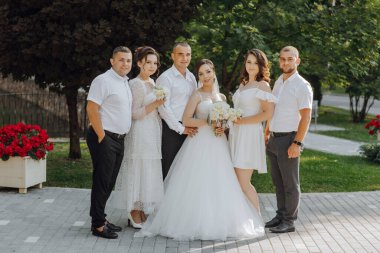 Gelin ve damat da dahil olmak üzere bir grup insan kaldırımda fotoğraf için poz veriyor.