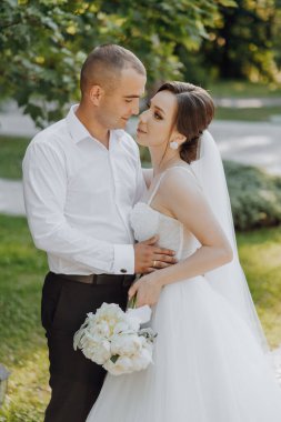 Gelin ve damat çimenli bir alanda, gelin bir buket tutuyor.