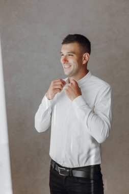 Beyaz gömlekli bir adam dışarı çıkmaya hazırlanıyor. Gülümsüyor ve keyfi yerinde.