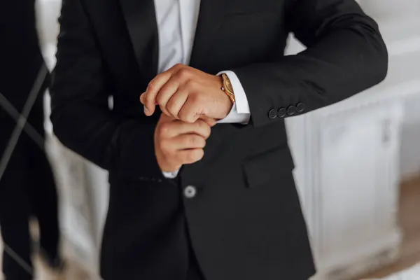 A man in a suit is wearing a gold watch and adjusting his cuff. Concept of formality and attention to detail, as the man takes care to ensure his appearance is polished and professional