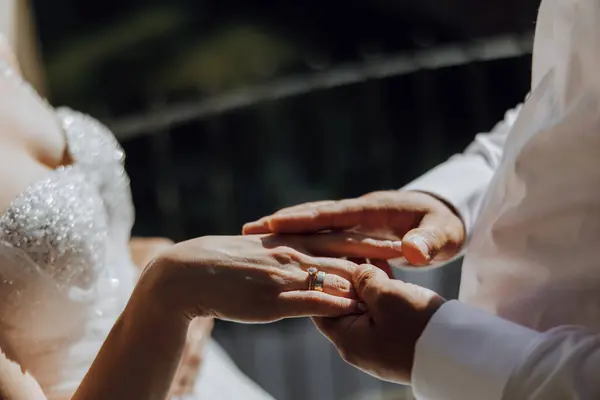 Bir gelin ve damat evleniyor ve yüzüklerini takmak üzereler. Gelin beyaz bir elbise giyiyor ve damat beyaz bir gömlek giyiyor.