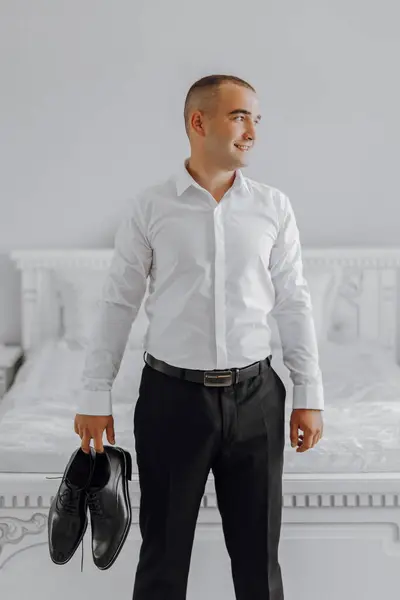Mężczyzna Białej Koszuli Czarnych Spodniach Trzyma Parę Butów Uśmiecha Się Zdjęcie Stockowe