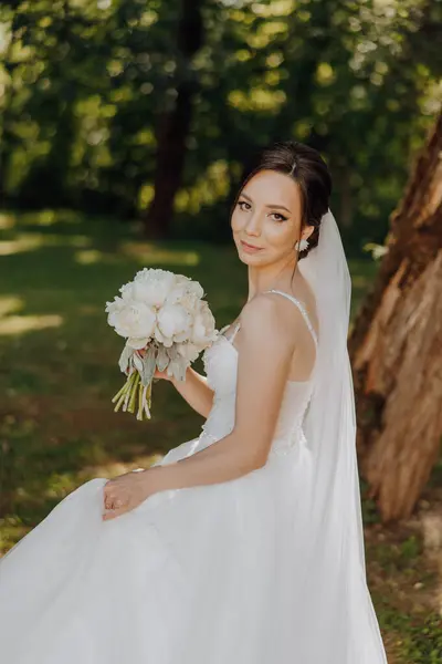 花束で写真を撮る花嫁がいる 彼女は白いドレスとベールを着ている 花嫁が彼女の結婚式の服を着ているので 幸せとお祝いの概念 ストック画像