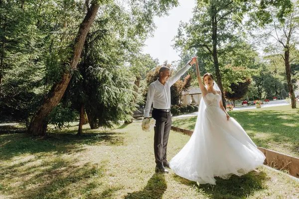 花嫁と花嫁が公園で踊っている 花嫁は白いドレスを着ていて グロムはスーツを着ています シーンは幸せでロマンチックです ロイヤリティフリーのストック画像