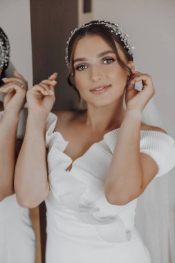 Beyaz bir elbise ve saç bandı takan bir kadın var. Gülümsüyor ve kameraya bakıyor.