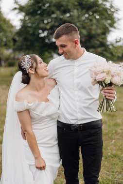 Bir gelin ve damat elinde çiçeklerle bir tarlada duruyorlar. Damat beyaz gömlek ve siyah pantolon giyerken gelin beyaz bir elbise ve bir saç bandı takıyor. Sahne mutlu ve kutlama dolu.