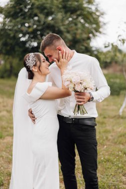 Gelin ve damat bir tarlada duruyorlar, gelin bir buket tutuyor ve damat bir buket tutuyor.