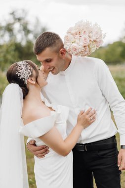 Bir gelin ve damat tarlada birbirlerine sarılıyorlar. Gelin beyaz bir elbise ve duvak takarken damat beyaz gömlek ve siyah pantolon giyiyor. İkisinin de elinde çiçekler var.