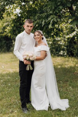 Bir gelin ve damat tarlada fotoğraf çektirmek için poz veriyorlar. Gelin beyaz bir elbise giyiyor ve damat beyaz bir gömlek giyiyor. Çiçek ve buket tutuyorlar. Sahne mutlu ve kutlama dolu.