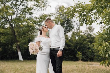 Gelin ve damat çimenli bir tarlada duruyorlar, gelin elinde buketle. Sahne romantik ve mutlu, çünkü çift düğün günlerini kutluyor.