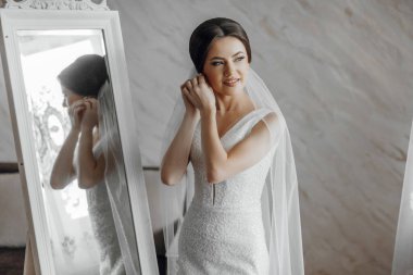 Bir kadın düğününe hazırlanıyor, duvağını takıyor ve aynadaki yansımasını kontrol ediyor.