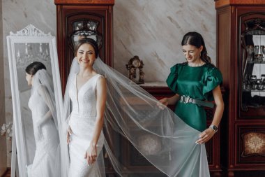 Gelinlik giymiş bir kadın, yeşil elbiseli bir kadın tarafından peçesini takıyor.