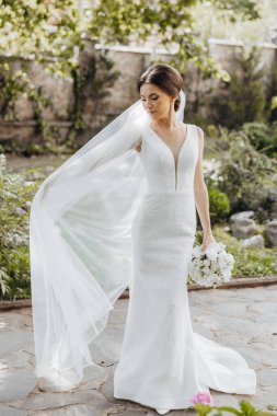 Beyaz elbiseli bir gelin saçında bir peçeyle yürüyor. Elinde bir buket çiçek tutuyor.