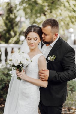 Gelin ve damat bir resim için poz veriyor, gelin bir buket çiçek tutuyor. Sahne mutlu ve romantik, çünkü çift düğün günlerini kutluyor.