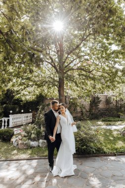 Bir gelin ve damat bir ağacın önünde el ele tutuşuyorlar. Aşk ve mutluluk kavramı, çift resmi giyinmiş ve bir resim için poz veriyor.