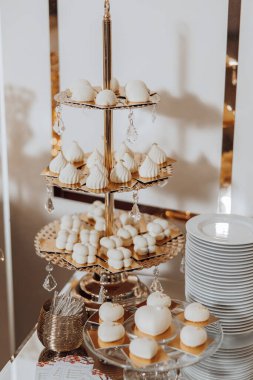 Pasta ve hamur işleri de dahil olmak üzere çeşitli tatlılar içeren üç kademeli bir tatlı sergisi. Sunum zarif ve davetkar, cam kapağı ve altın çerçevesi var.