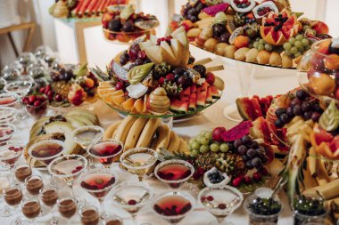 Şarap bardakları ve martini bardakları dahil, meyve ve içeceklerle dolu bir masa. Meyve, onu açık büfe gibi gösterecek şekilde düzenlenmiş.