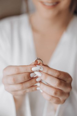 Bir kadın elinde bir yüzük tutuyor. Yüzük elmas bir yüzük ve o gülümsüyor.