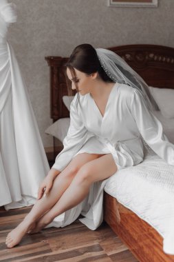 Beyaz bornozlu bir kadın yatağa oturur. Duvak takıyor ve bacak bacak üstüne atıyor. Oda beyaz bir şifonyer ve ahşap bir yatak ile süslenmiş.