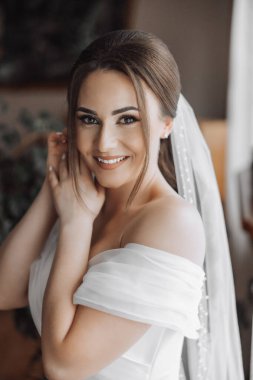 Kafasında beyaz bir duvak olan bir kadın resim için poz veriyor. Gülümsüyor ve kameraya bakıyor.