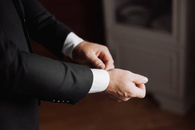 Takım elbiseli bir adam giyinmeye hazırlanıyor. Gömleğini ve kollarını düzeltiyor.