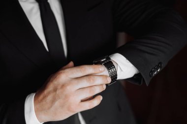 Takım elbiseli bir adam saat takıyor ve ayarlıyor. Formalite ve detaylara dikkat etme kavramı. Çünkü adam saatinin düzgün ayarlandığından emin olmak istiyor.