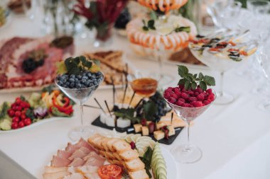 Çeşitli yiyecek ve içeceklerle dolu bir masa, ahududu ve yaban mersinli bir meyve tabağı da dahil.