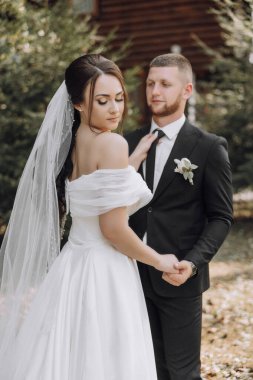 Bir gelin ve damat evin önünde duruyorlar. Gelin beyaz bir elbise giyiyor ve damat siyah bir takım giyiyor.