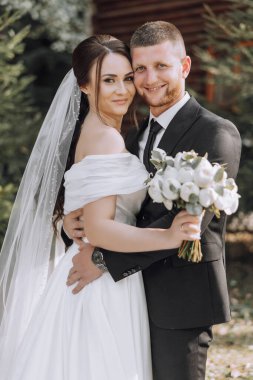Bir gelin ve damat bir buket çiçekli fotoğraf için poz veriyorlar. Gelin beyaz bir elbise giyiyor ve damat bir takım elbise giyiyor. Sahne mutlu ve kutlama dolu.