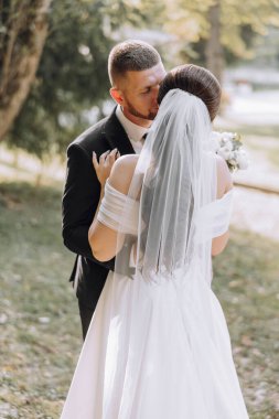 Bir gelin ve damat çimen tarlasında sarılıyorlar. Gelin beyaz bir elbise giyiyor ve damat siyah bir takım giyiyor.