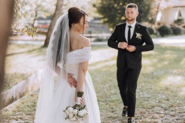 Gelin ve damat parkta duruyorlar, gelin elinde bir buket çiçekle.