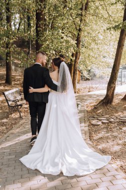 Bir gelin ve damat parkta bir patikada yürüyorlar. Gelin beyaz bir elbise giyiyor ve damat bir takım elbise giyiyor. El ele tutuşup kameraya gülümsüyorlar. Sahne mutlu ve romantik.