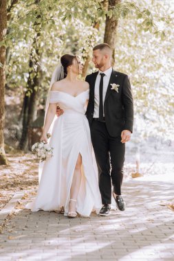 Gelin ve damat, gelin elinde buketle bir patikada yürüyorlar. Sahne mutlu ve romantik, çünkü çift düğün günlerini kutluyor.