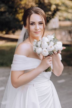 Bir kadın elinde bir buket beyaz çiçek tutuyor. Beyaz bir elbise ve duvak takıyor. Çiçekler bir vazoya konur ve onun eline yerleştirilir. Sahne muhtemelen bir düğün ya da özel bir olay.