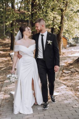 Bir gelin ve damat yolda yürüyorlar, gelin bir buket tutuyor ve damat kravat takıyor.