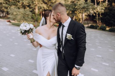 Gelin ve damat kaldırımda yürürken gelin elinde bir buket çiçek tutuyordu. Sahne mutlu ve romantik.