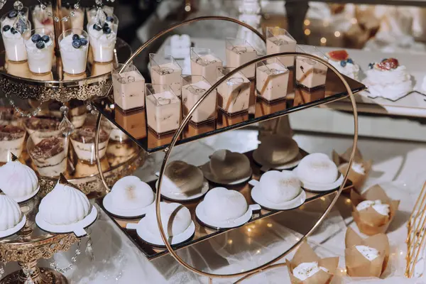 Pastalar, pastalar ve diğer tatlılarla dolu bir masa. Tatlılar altın tepside sergileniyor ve onları lezzetli ve cezbedici gösterecek şekilde sergileniyor.