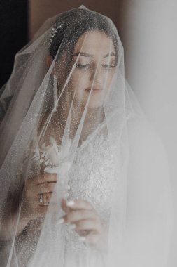 Bir kadın peçe takıyor ve elinde bir çiçek tutuyor. O, kameraya bakıyor. Duvak beyaz ve ışıltılı bir etkisi var.