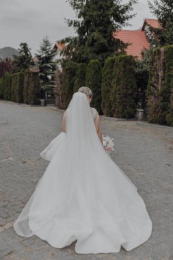 Beyaz gelinlikli bir kadın caddede yürüyor. Elinde bir buket çiçek tutuyor.