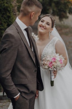 Bir gelin ve damat fotoğraf için poz veriyor. Gelin elinde bir buket çiçek tutuyor.